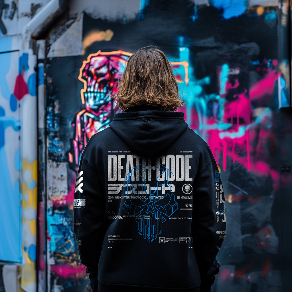 Person wearing a black hoodie with 'DEATH CODE' design in front of colorful graffiti.